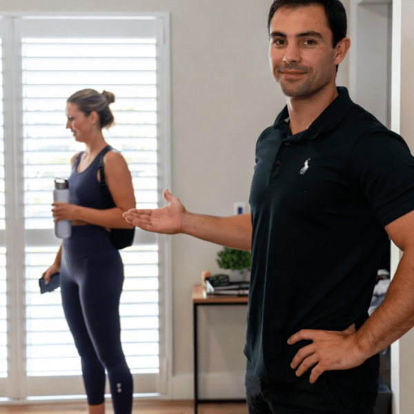 Female patient smiles while a male physiotherapist in a black polo shirt gently guides her straight arm through a shoulder assessment in a bright, modern clinic room at Specific Physiotherapy Preston – representing expert local physiotherapy care.