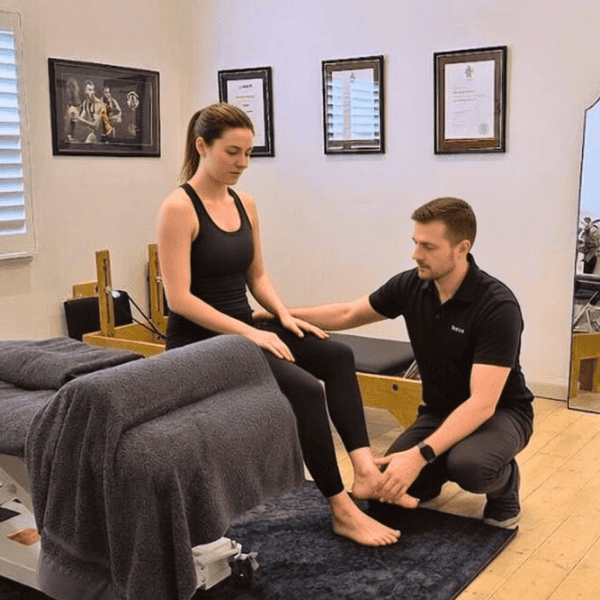 Male physiotherapist in black polo performing hands-on plantar fasciitis assessment on female patient in activewear at Specific Physiotherapy clinic in Preston VIC. Expert foot and ankle examination for heel pain relief after summer walks – serving Preston, Reservoir, Thornbury, and Northcote.